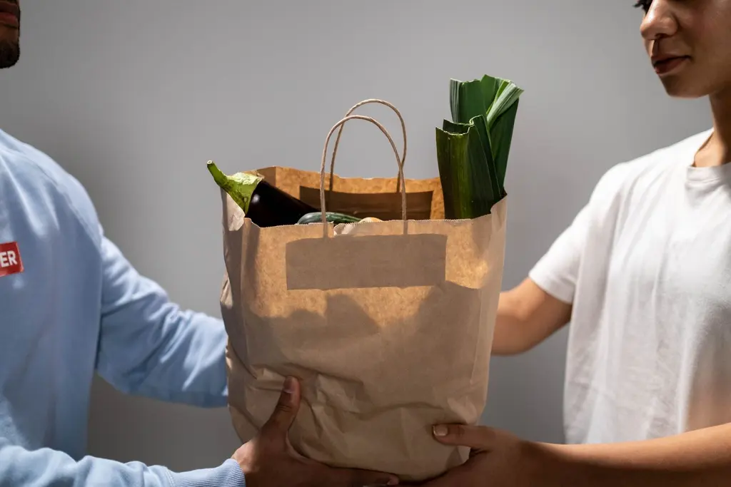 Hands passing a paper bag of fresh vegetables