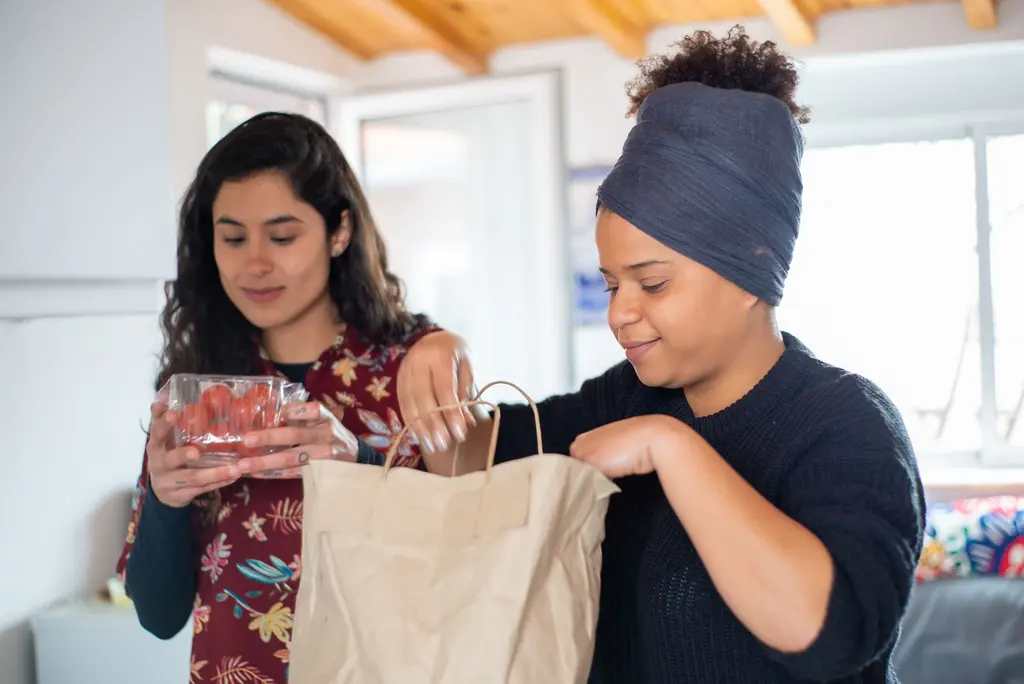 Two women unpacking a paper bag of groceries at home